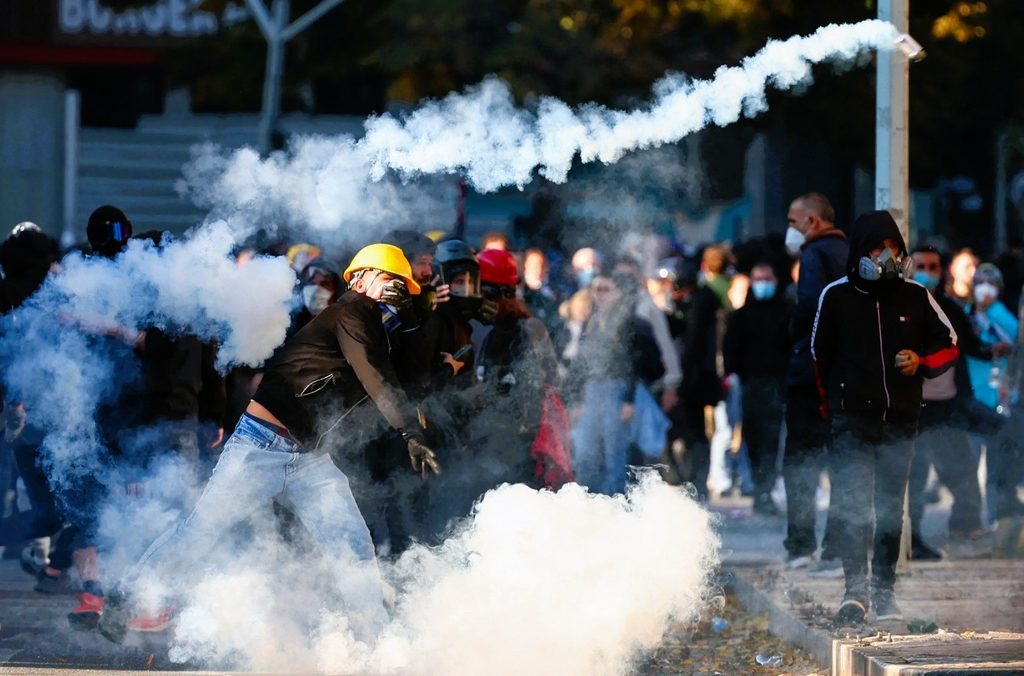 Primary Image Alt Text (if assigned):

Albanian riot police holding shields under falling fireworks and tear gas smoke outside parliament in Tirana during the 8th day of protests