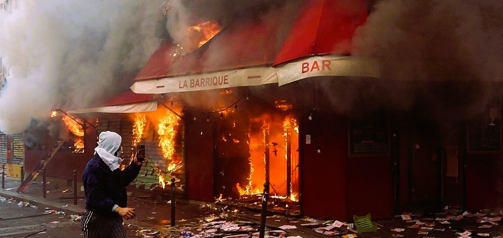 Firefighters extinguishing a burnt-out car along a littered Paris boulevard following overnight riots and looting