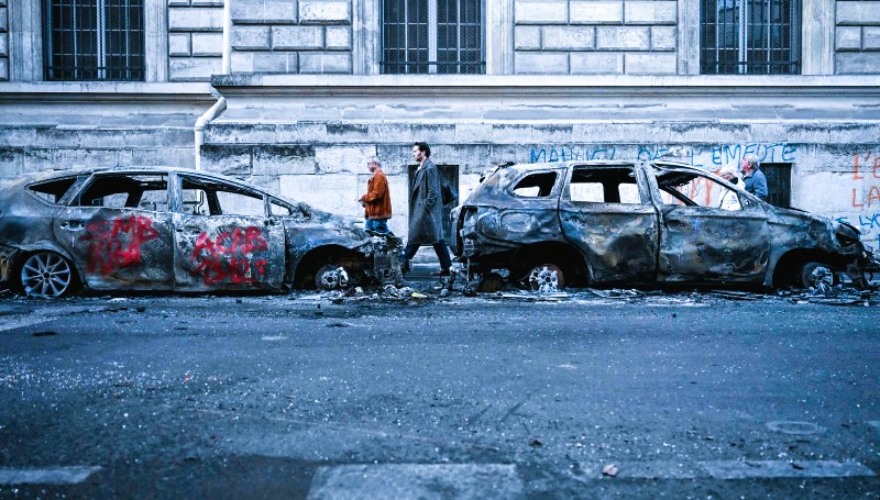Firefighters extinguishing a burnt-out car along a littered Paris boulevard following overnight riots and looting